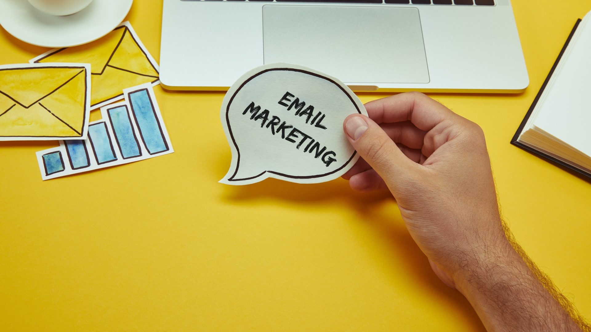 cropped image of man holding speech bubble with"email marketing" lettering near laptop
