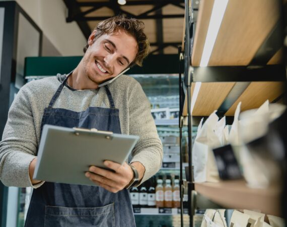 Smiling busy bartender checking goods while talking on phone in small cafeteria